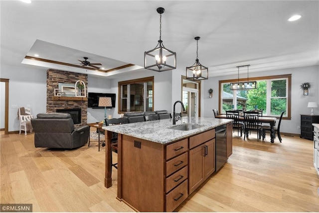 3735 Crest Ridge Ct, Eau Claire, WI 54701 - kitchen with dishwashing machine, a stone fireplace, light wood-type flooring, brown cabinetry, and hanging light fixtures