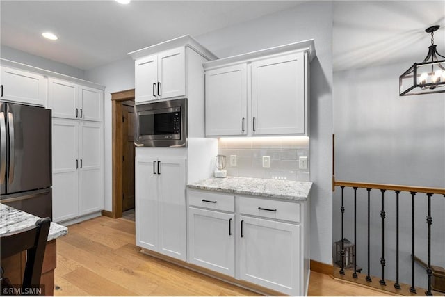 3735 Crest Ridge Ct, Eau Claire, WI 54701 - kitchen featuring stainless steel microwave, freestanding refrigerator, white cabinets, light wood-type flooring, and backsplash