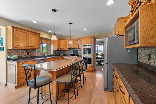 1948 Field Cliffe Dr, Richfield, WI 53076 - kitchen featuring appliances with stainless steel finishes, a breakfast bar area, light wood-style floors, decorative backsplash, and an island with sink