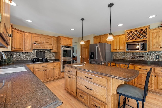 1948 Field Cliffe Dr, Richfield, WI 53076 - kitchen featuring appliances with stainless steel finishes, a center island with sink, tasteful backsplash, light wood finished floors, and a breakfast bar