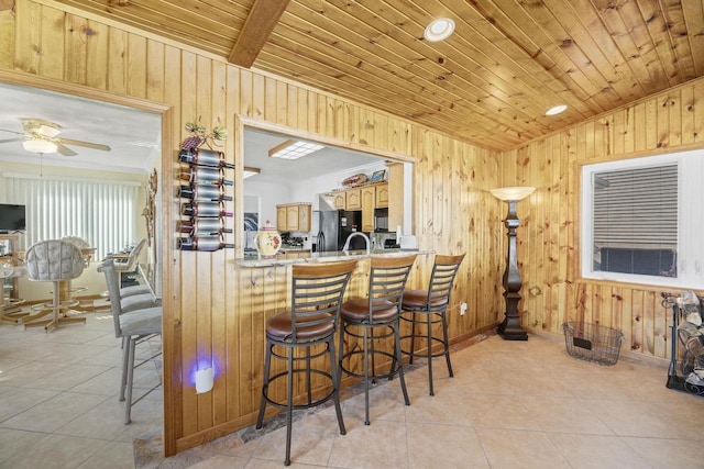 442 E Richardson Springs Rd, Edgerton, WI 53534 - kitchen featuring black appliances, wood walls, light tile patterned floors, ceiling fan, and a kitchen breakfast bar