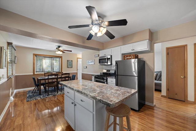 4683 N 80th St, Milwaukee, WI 53218 - kitchen with stainless steel appliances, a kitchen island, white cabinets, light wood-type flooring, and a ceiling fan