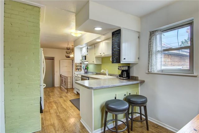 1418 Keith St, Eau Claire, WI 54701 - kitchen featuring white microwave, range, light wood-type flooring, a kitchen breakfast bar, and light countertops