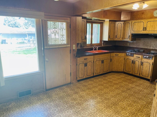 5734 N 80th St, Milwaukee, WI 53218 - kitchen with dark countertops, range hood, stainless steel gas stovetop, brown cabinetry, and tasteful backsplash