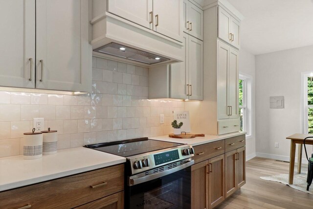 1108 Heritage Ct, Waunakee, WI 53597 - kitchen featuring stainless steel range with electric stovetop, premium range hood, light wood-style floors, light countertops, and backsplash