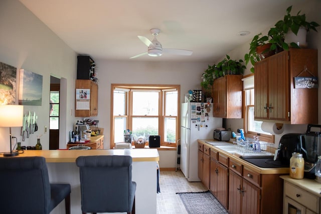 N65W35097 Rd J, Oconomowoc, WI 53066 - kitchen with freestanding refrigerator, ceiling fan, light countertops, and brown cabinetry