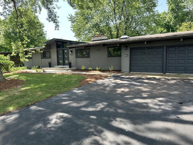 8221 Fairmont Ln, Greendale, WI 53129 - view of front facade with asphalt driveway, an attached garage, a chimney, and a front lawn