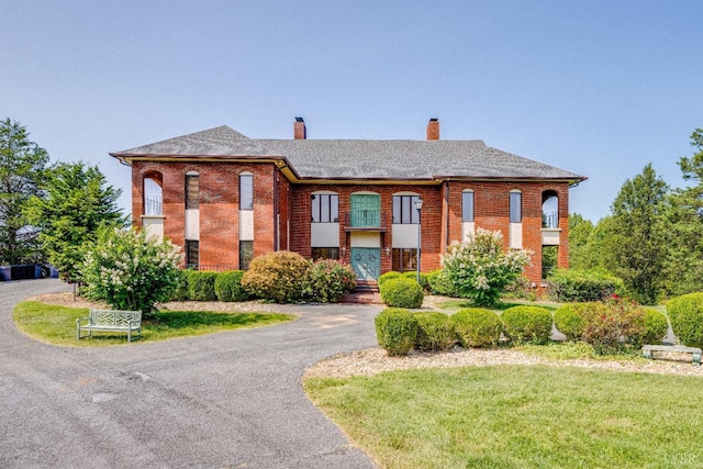 view of front of property with brick siding, a front lawn, aphalt driveway, and a chimney