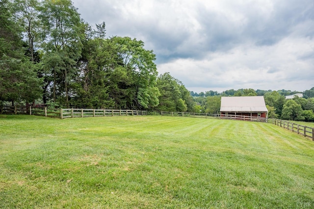 view of yard featuring fence, an exterior structure, an outdoor structure, and a rural view