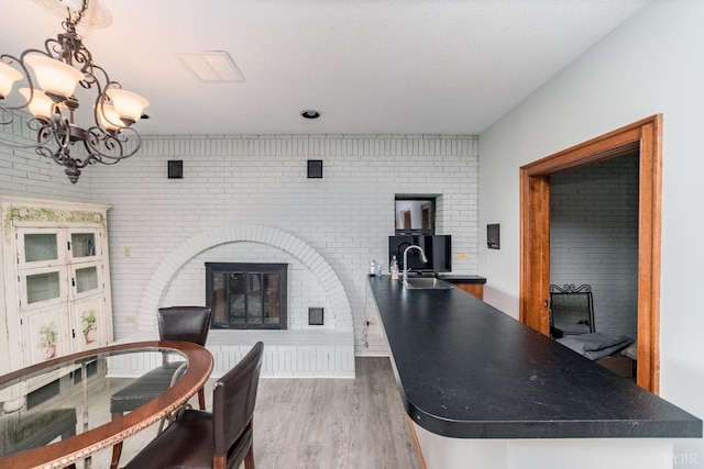 dining space featuring brick wall, light wood-style floors, a glass covered fireplace, and a chandelier