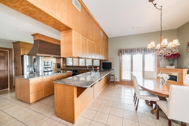 kitchen with a peninsula, appliances with stainless steel finishes, a sink, an inviting chandelier, and light tile patterned floors