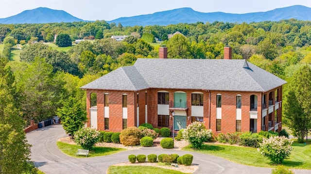 view of front of house featuring brick siding, a mountain view, curved driveway, and a forest view