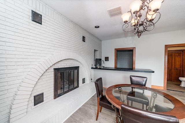 dining area featuring an inviting chandelier, a textured ceiling, visible vents, a brick fireplace, and wood finished floors