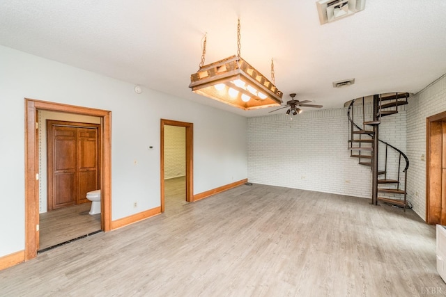 interior space with ceiling fan, visible vents, brick wall, and light wood finished floors