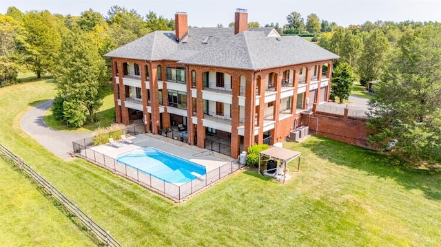 rear view of property with a community pool, a patio area, a chimney, a lawn, and central AC