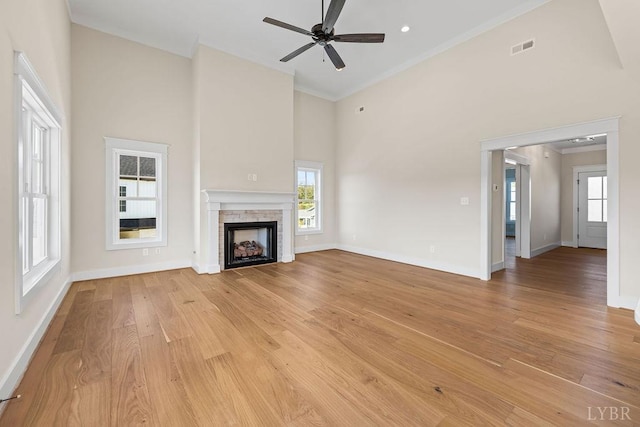 unfurnished living room featuring light wood-style flooring, baseboards, ceiling fan, crown molding, and a high ceiling