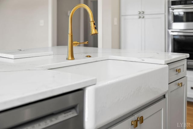 details with a sink, stainless steel double oven, light stone counters, dishwasher, and white cabinets