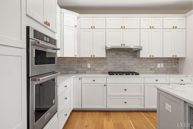 kitchen featuring light wood finished floors, gas stovetop, stainless steel double oven, white cabinetry, and under cabinet range hood