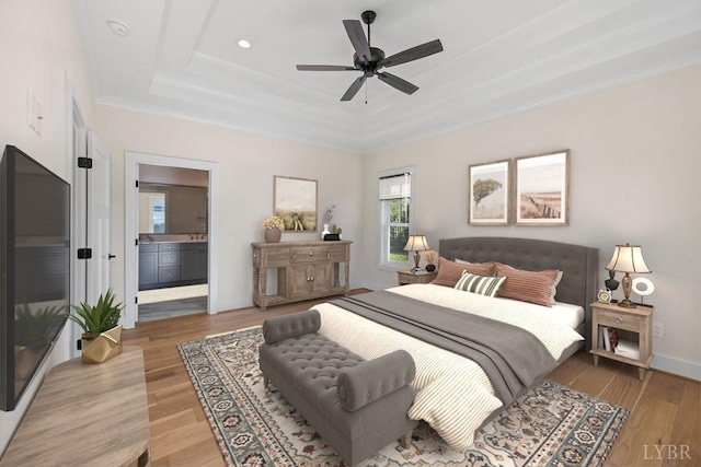 bedroom featuring baseboards, ensuite bathroom, ceiling fan, a raised ceiling, and light wood-type flooring