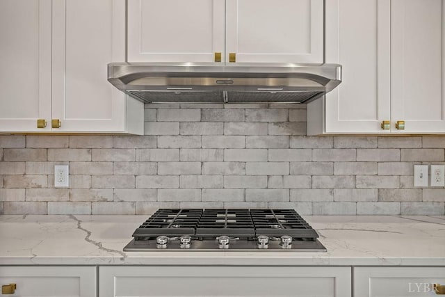 interior details with under cabinet range hood, white cabinets, decorative backsplash, and stainless steel gas stovetop