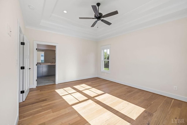unfurnished room featuring ornamental molding, a ceiling fan, a raised ceiling, baseboards, and light wood-style floors
