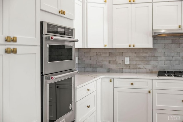 kitchen featuring light stone countertops, white cabinets, black gas cooktop, double oven, and tasteful backsplash