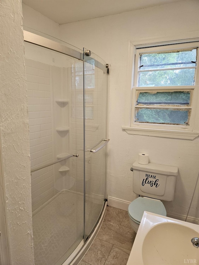 full bathroom featuring toilet, baseboards, a stall shower, and a sink