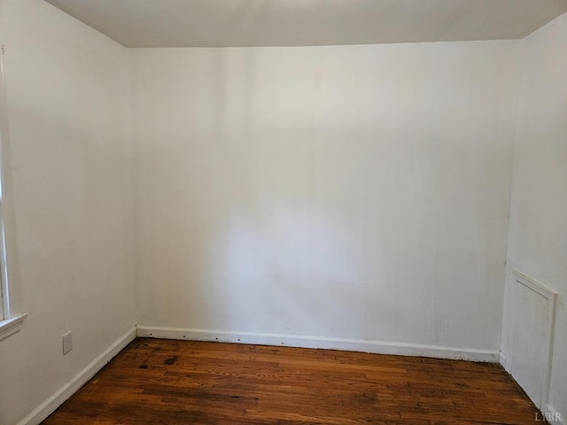 spare room featuring baseboards and dark wood finished floors