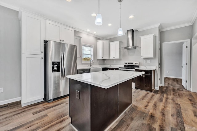 kitchen with ornamental molding, wood finished floors, wall chimney range hood, and stainless steel appliances