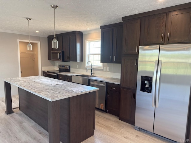 kitchen with stainless steel appliances, a sink, light wood finished floors, a kitchen island, and crown molding