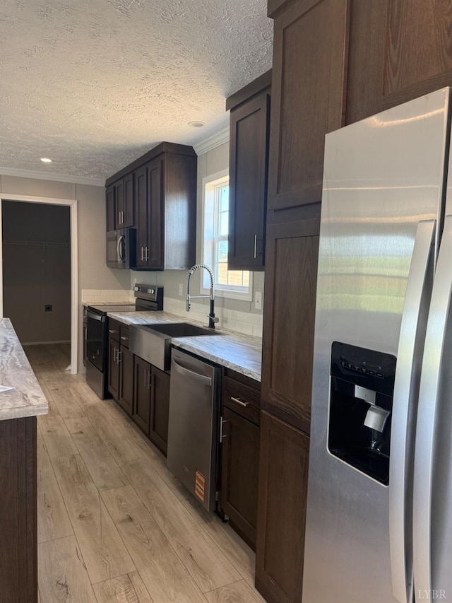 kitchen featuring stainless steel appliances, crown molding, a sink, light wood-type flooring, and a textured ceiling