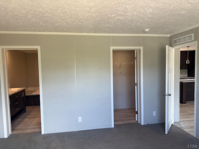 unfurnished bedroom featuring a textured ceiling, a spacious closet, carpet flooring, a closet, and ornamental molding