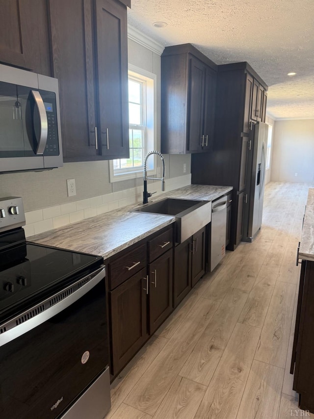 kitchen with stainless steel appliances, a sink, light wood-type flooring, ornamental molding, and a textured ceiling