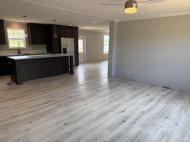 kitchen featuring open floor plan, crown molding, a textured ceiling, light wood finished floors, and plenty of natural light