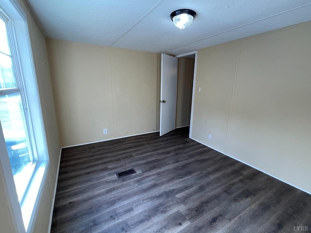 empty room featuring plenty of natural light, dark wood-type flooring, and a textured ceiling