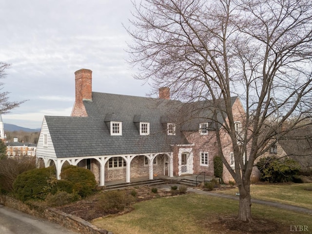new england style home with a front lawn, a porch, a chimney, and stone siding