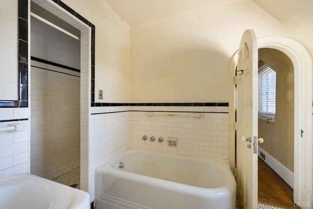 bathroom with a garden tub, tile walls, and wainscoting