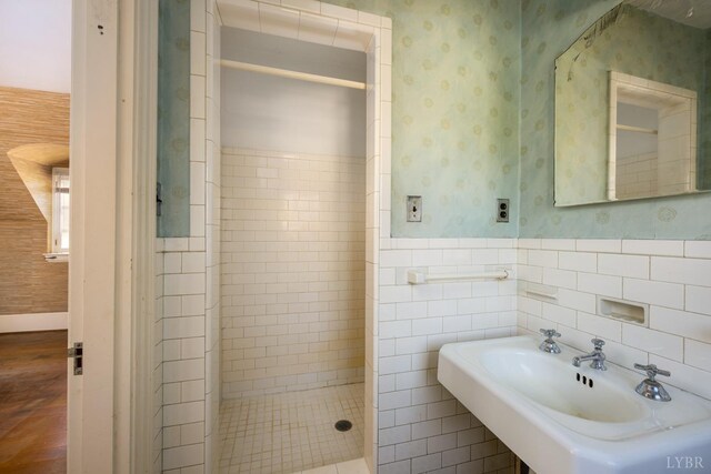 full bath featuring a sink, a wainscoted wall, wood finished floors, tiled shower, and wallpapered walls