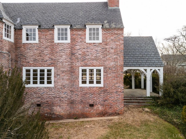 view of side of home featuring a high end roof, brick siding, crawl space, and a chimney