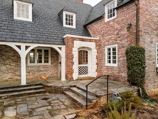property entrance with a chimney, a high end roof, and brick siding