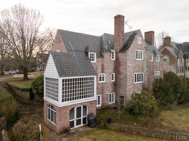 rear view of property with a high end roof, a chimney, and brick siding