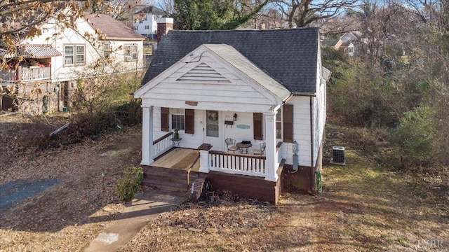 bungalow-style home with cooling unit, a porch, and a shingled roof