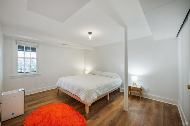 bedroom featuring hardwood / wood-style floors, concrete block wall, and baseboards