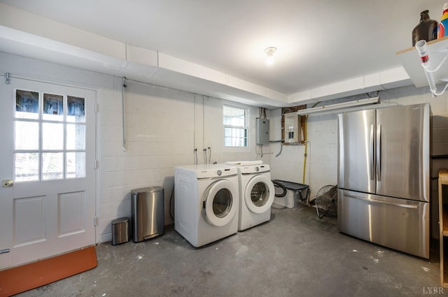 laundry area featuring electric panel, washer and clothes dryer, and concrete block wall