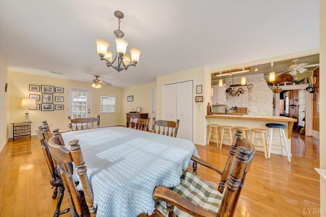 dining space with a chandelier, light wood-style flooring, a ceiling fan, and baseboards
