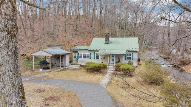 view of front of property featuring driveway, covered porch, a chimney, metal roof, and a carport