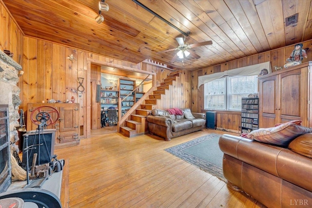 living room with wooden walls, wooden ceiling, stairway, light wood-type flooring, and ceiling fan