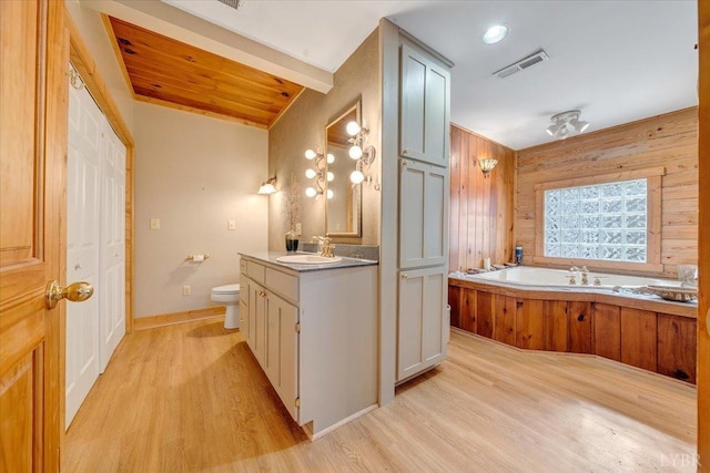 bathroom with wood finished floors, toilet, vanity, a garden tub, and wood walls