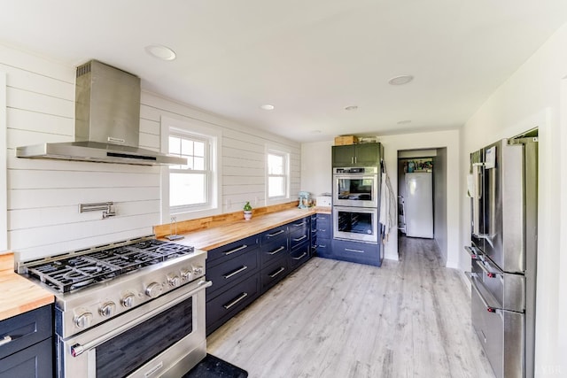 1038 Valencia Dr, Huddleston, VA 24101 - kitchen featuring stainless steel appliances, wall chimney exhaust hood, butcher block countertops, light wood-style flooring, and blue cabinetry