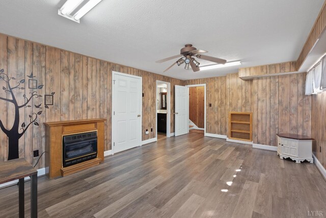337 Virginia Ave, Appomattox, VA 24522 - unfurnished living room featuring a ceiling fan, a glass covered fireplace, wood walls, wood finished floors, and baseboards